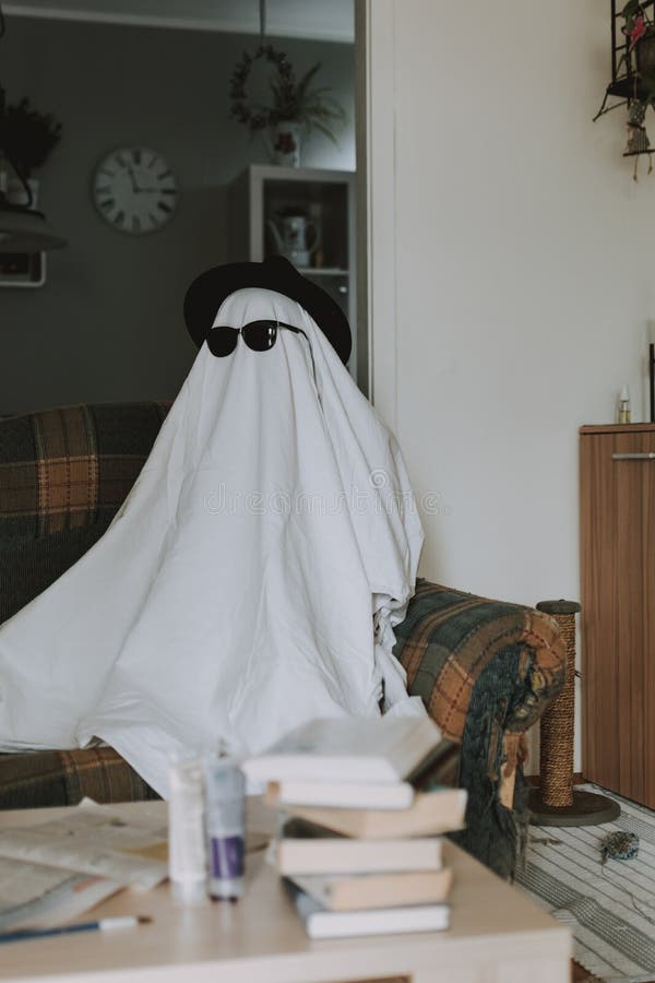 person-wearing-white-bedsheet-over-his-head-hat-sunglasses-like-ghost-sitting-couch-201489851.jpg
